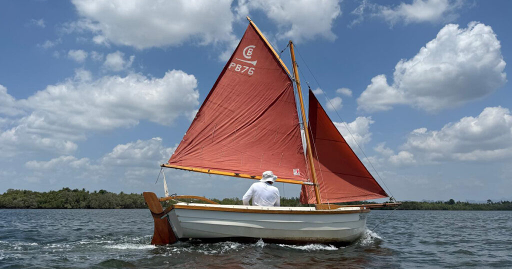 Post Boat with red sails crossing open estuary water in Krabi