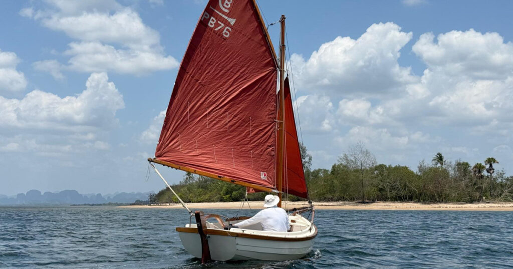Post Boat sailing away beside the Krabi shoreline under red sails